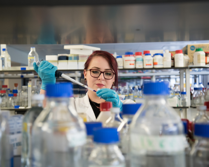 A female student working in a lab, with an array of bottles on shelves in front of her and behind her