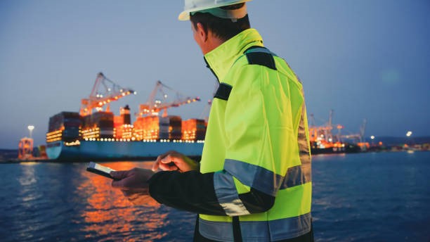 A man in a high vis jacket looking at a cargo ship