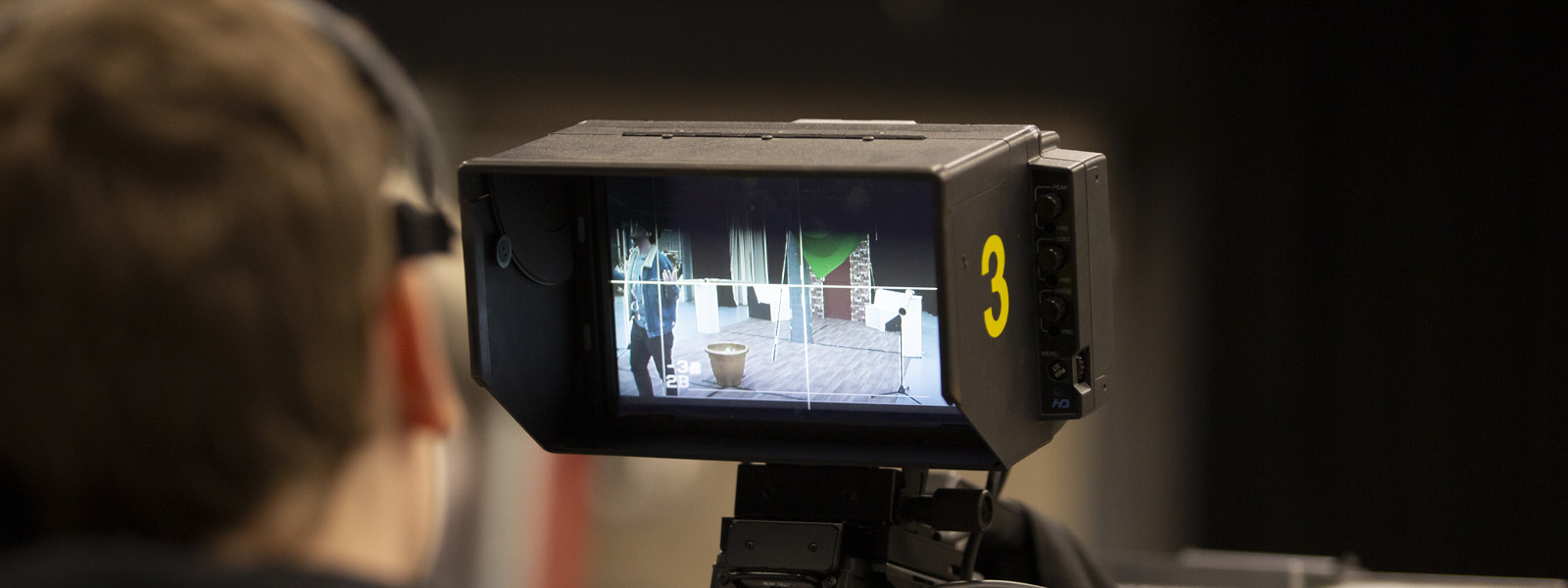 A student looking through the lens of a television camera in a studio