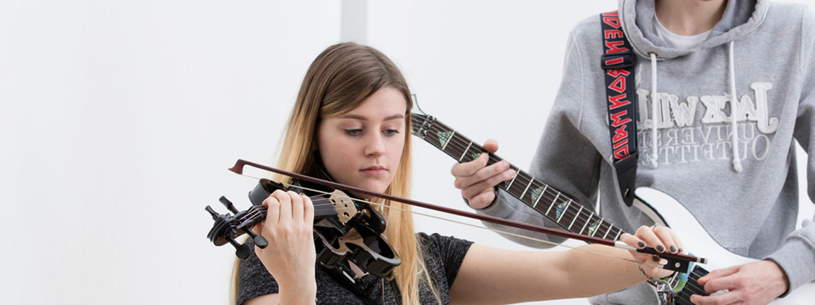 Male student playing electric guitar alongside female student playing a violin