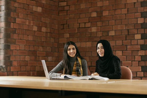 two students smiling at the camera with a laptop in front of them