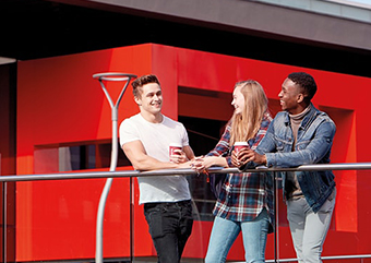 Three students leaning on a railing and chatting outside Towers