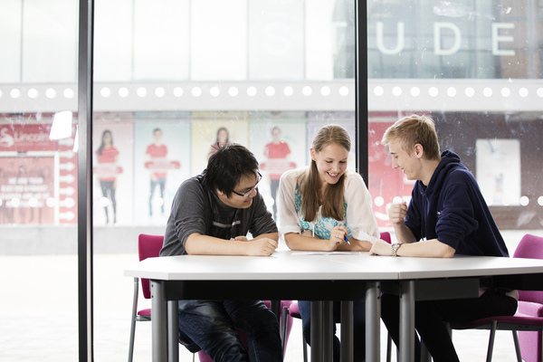 Three students sat at a table reading a book