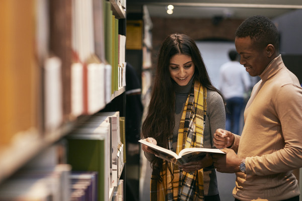 Two students looking at a book together in the Great Central Warehouse Library