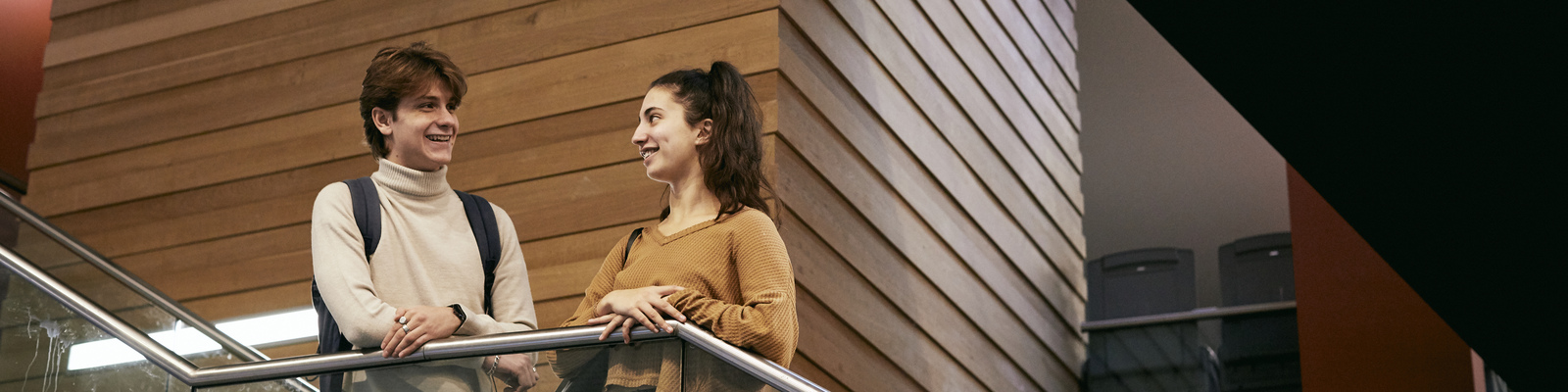 Male and female student stood next to one another in building on campus