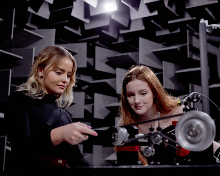 Students interacting with engineering equipment in semi-anechoic chamber.