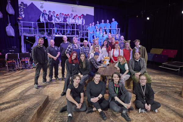 A group of students and staff involved in a theatre production posing together on stage