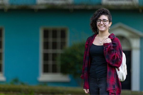 A student stood smiling in front of a blue house