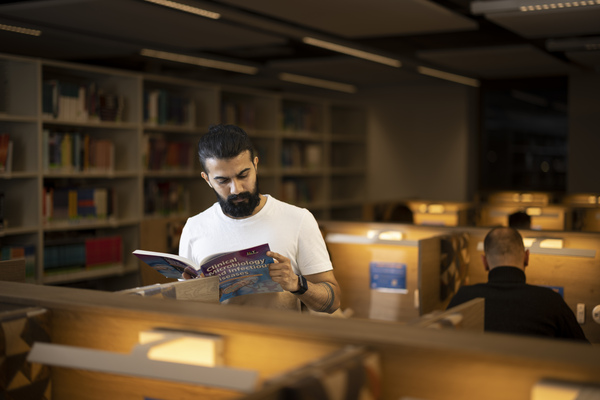 Student stood reading a book in the Ross Library