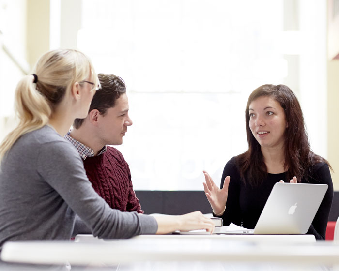 A group of students sat talking at a desk with a laptop