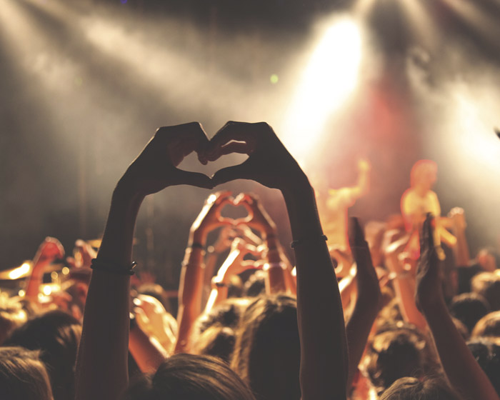 A pair of hands making a heart shape from the audience at a concert