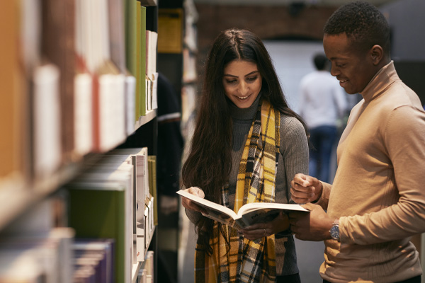 Two students chatting and reading a book in the library