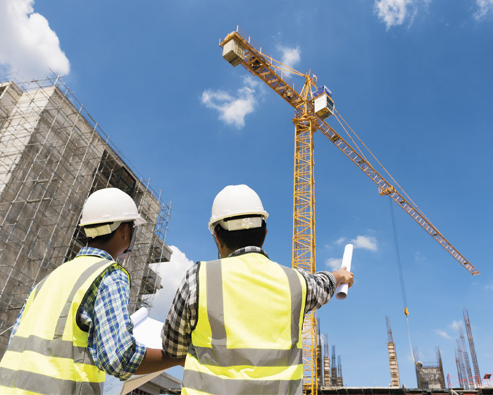 Two site workers in hi-vis jackets on a construction site with a crane in the background