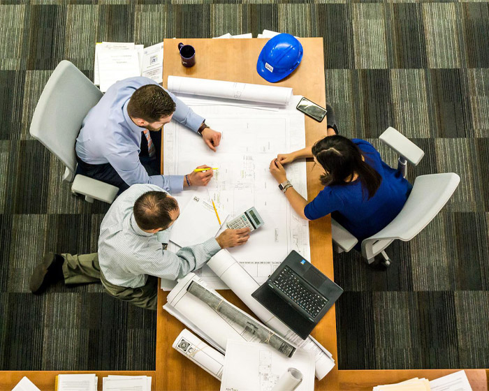 Three people sat around a desk examining a set of plans