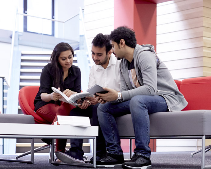 Three students reading a book together in a seminar room