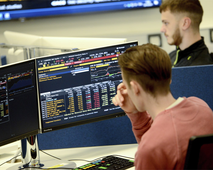 A student sitting in front of two computer screens displaying financial information