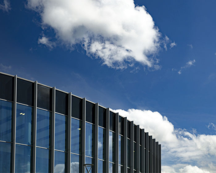 The outside of a glass building with blue sky and clouds