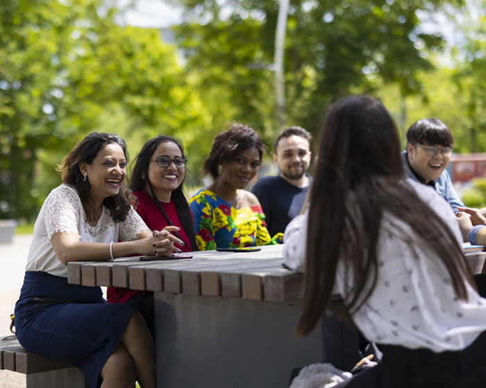 A group of students sat on a bench outside on campus