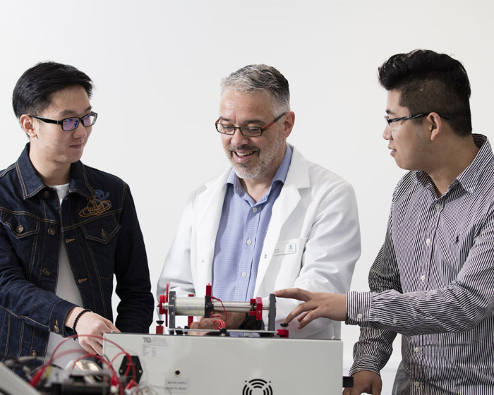 A member of staff explaining how an electronic item works to two students in a lab