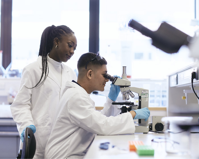 Two students working in a science lab with one of the students using a microscope