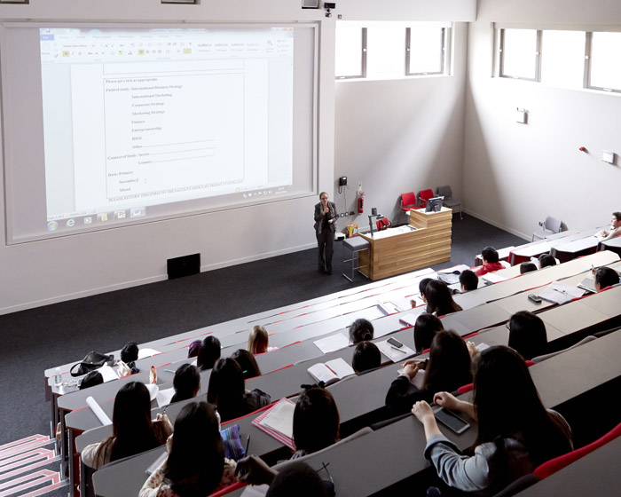 A lecturer presenting to students in a large lecture theatre