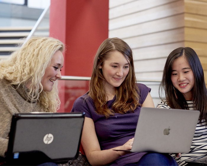 Three students working on laptops in a seminar room
