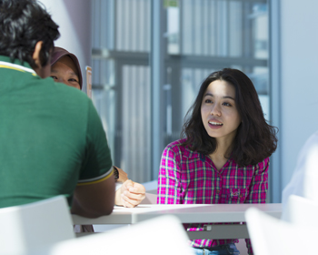 A group of three students sat at a table in the Isaac Newton Building, having a conversation