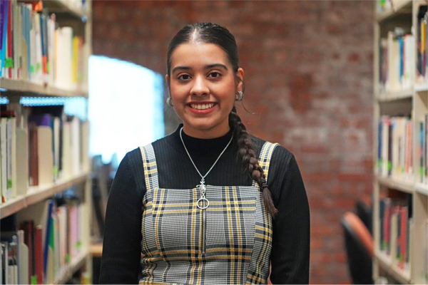 A woman stood in the library with a bookshelf next to her