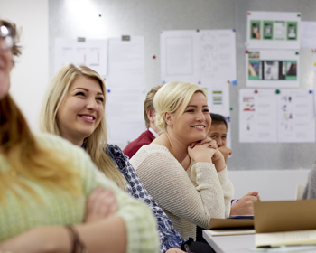 A group of people sat at a desk with notepads, listening to a speaker