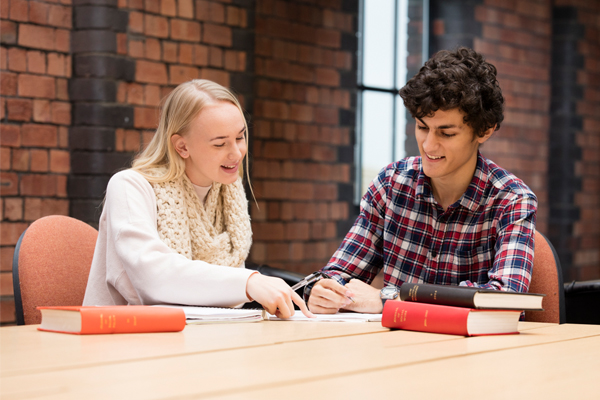 Two students sat smiling with a book