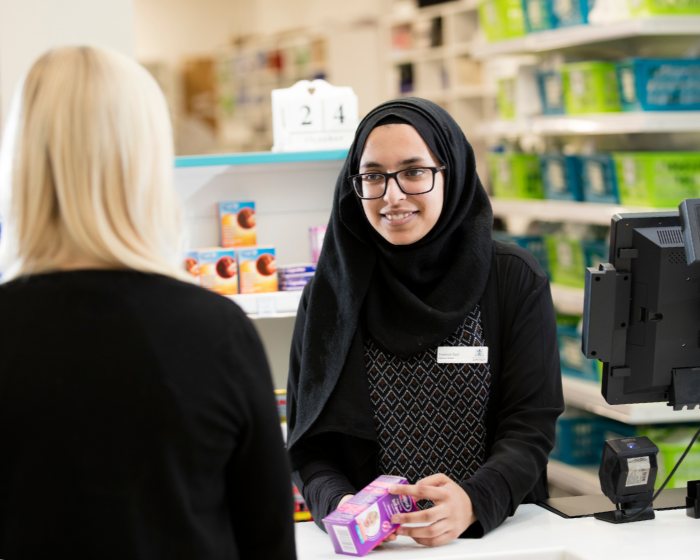 A pharmacist holding some medicine and speaking over a counter with a patient