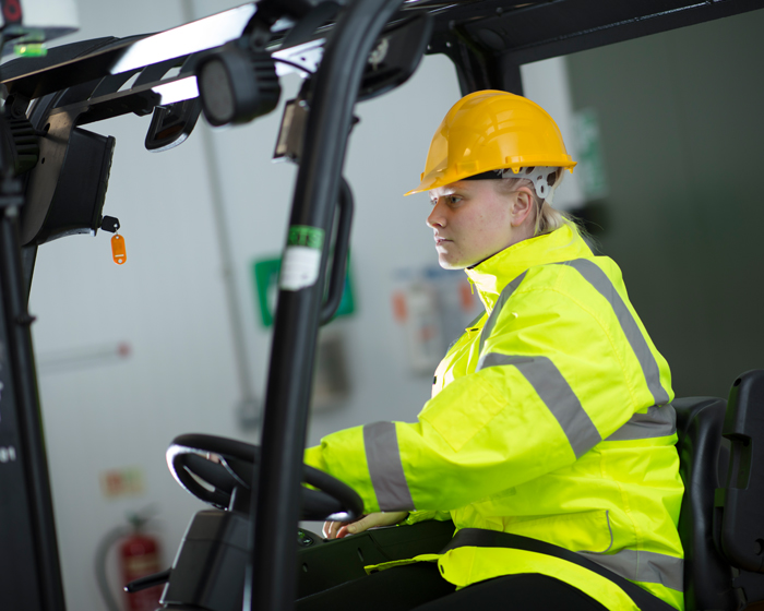 Forklift driver in a green high vis coat and yellow hard hat