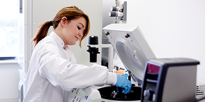 Female student in a white lab coat using lab equipment