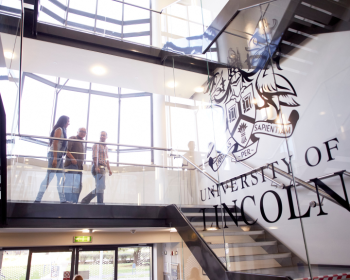 Three students walking down the staircase in the Joseph Banks Laboratories, with a large University of Lincoln crest on the wall to the right