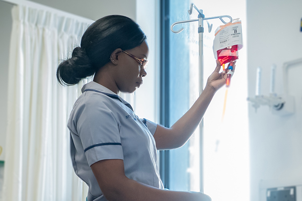 A nurse checking an IV bag with red fluid