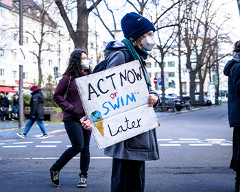 PROTESTER HOLDING A SIGN THAT READS, 'ACT NOW OR SWIM LATER'.