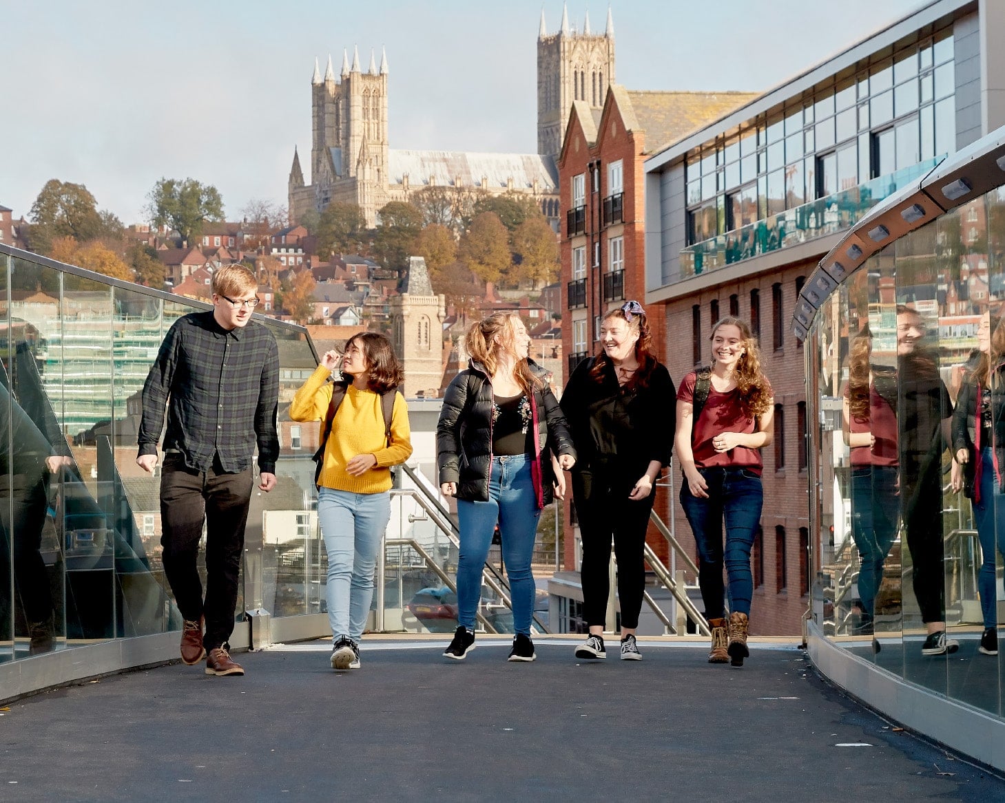 Five students walking across a footbridge, with Lincoln Cathedral visible in the background