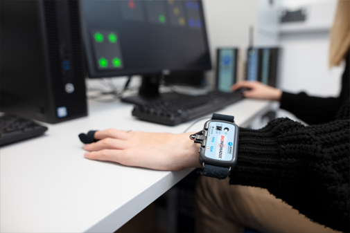 Student working on a cognition experiment on a desktop PC, with monitoring equipment on their finger and wrist