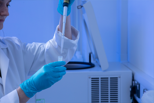 Student in white lab coat and blue globes measuring cortisol levels in lab with a pipette and test tube