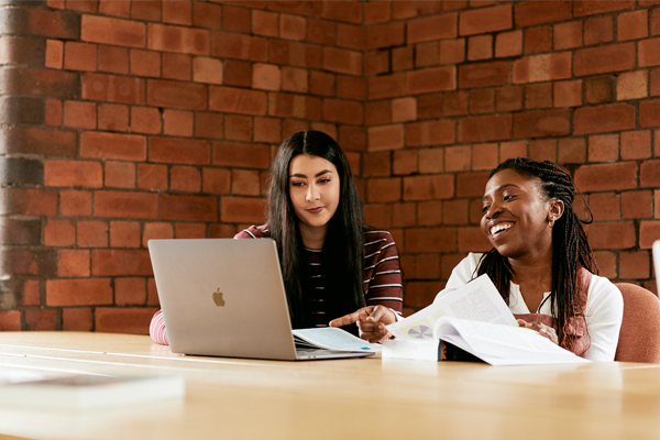 Two female students sat at a table with a laptop