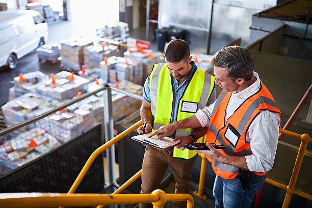 Two factory workers stood in front of a boxes looking at a tablet