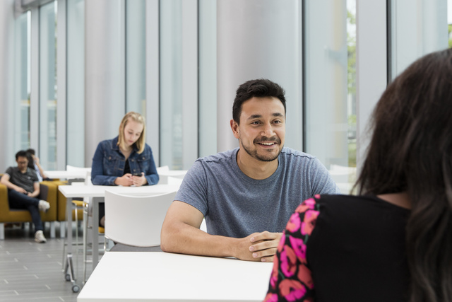 Students chatting in the Isaac Newton Building sat at a table