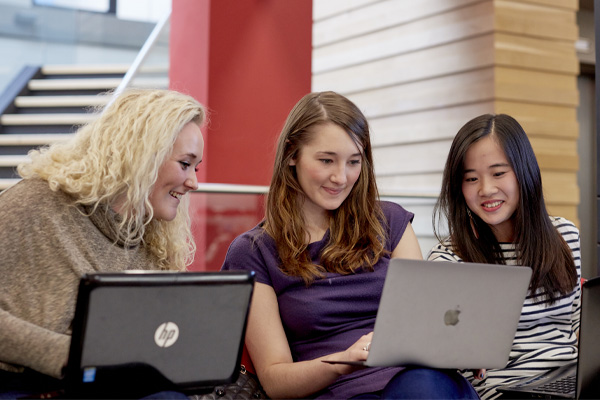 Three students working on laptops in a seminar room