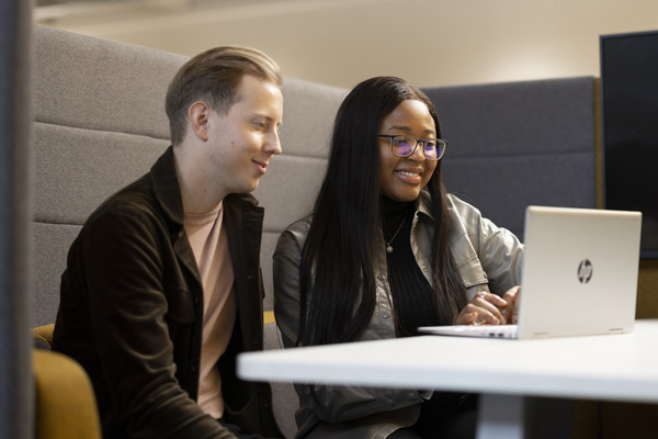 Two students working on a laptop in a study space