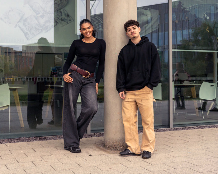 Two students leaning up against a pillar outside a glass building