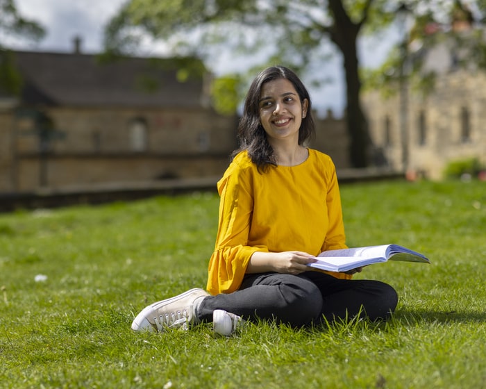 A student reading a text book on a grass lawn