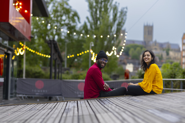 Two students sat outside Tower Bar, there are string lights in the background.