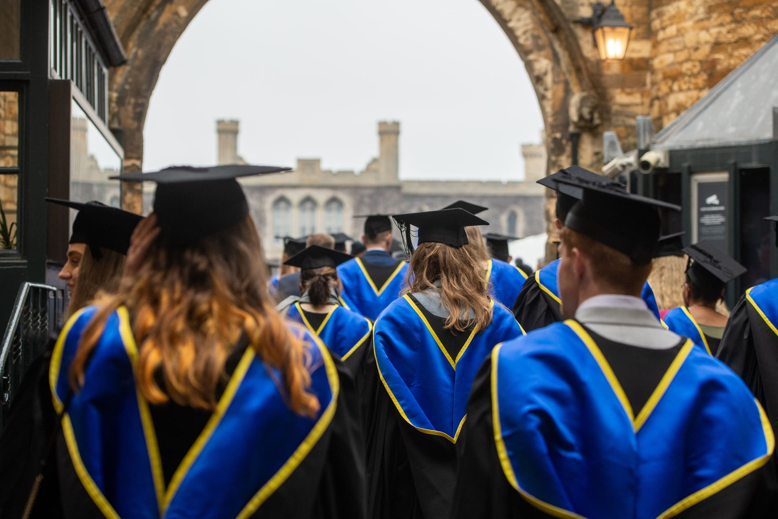 Students in graduation caps, gowns, and hoods, walking into the grounds of Lincoln Castle