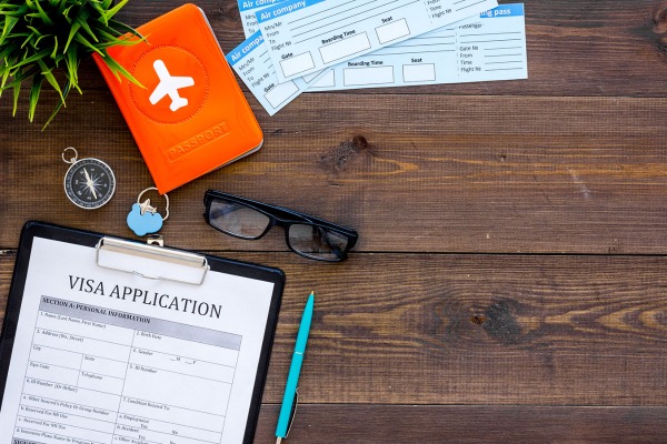 A visa application form is on a desk next to airline tickets