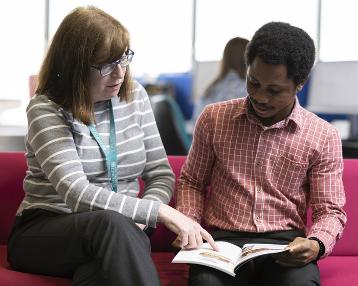 A tutor points at something in a book for a student